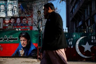 People walk past a banner with a picture of the former Prime Minister Imran Khan outside the party office of Pakistan Tehreek-e-Insaf, a day after the general election, in Lahore, Pakistan | Photo: Reuters